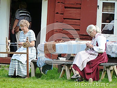 Women sewing dressed in old costumes outside old red barn in Sweden Editorial Stock Photo