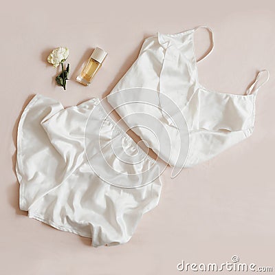 Women silk lingerie, perfume and a rose on beige background, flatlay, top view. Female elegant lace nightwear clothes. Stock Photo