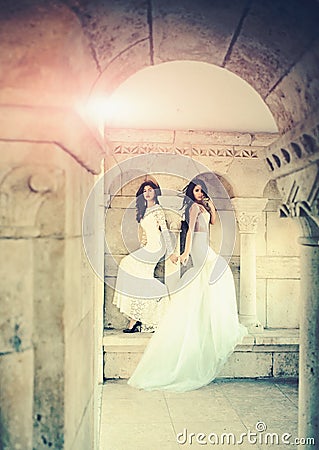 Women at stone ancient arch in summer. Sexy girls in white dress with stylish hair. Fashion model or princess in dress Stock Photo