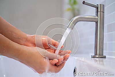 Women turn on the water to wash their hands in the bathroom. Frequent hand washing to help clean, reduce the accumulation of Stock Photo