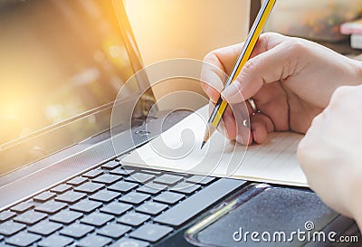 Women are using pencil to write books. Placed on a notebook computer. Light yellow tone Stock Photo