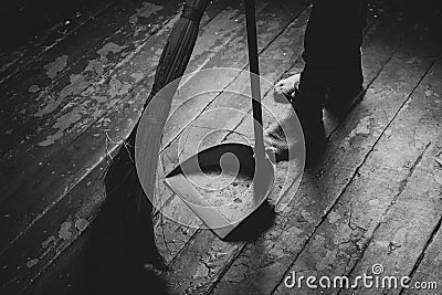 Women's feet on the floor and a broom and dustpan nearby, a girl sweeping the floor of the house, black and white Stock Photo