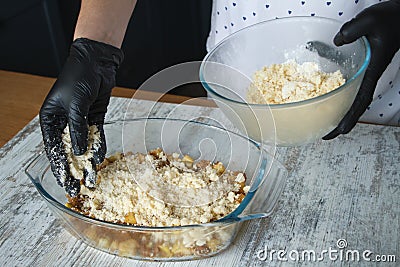 Womens black-gloved hands make apple crisp pie, put dough crumbs on grated apple Stock Photo