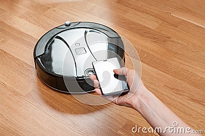 womens hand using mobile to control black robotic vacuum cleaner. modern smart cleaning technology. easier, safer and smarter way Stock Photo