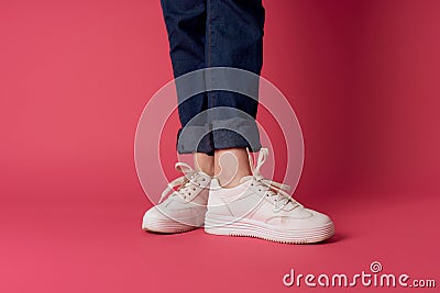 Womens legs jeans white sneakers street fashion studio pink background Stock Photo