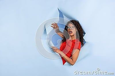 Cheerful young woman poses in torn blue paper hole background, emotional and expressive Stock Photo