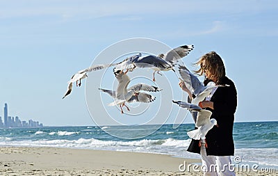 Happy healthy mature woman hand feeding seagulls birds on beach Stock Photo