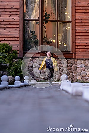 Wonderful little lady running on street to camera with joyful smile shining on face, spending active walk near house. Stock Photo