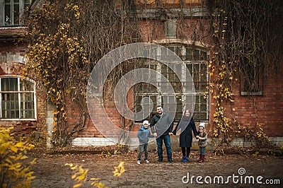 A wonderful sweet family stands near an old brick house in the fall, they hold hands and smile. Soft focus Stock Photo