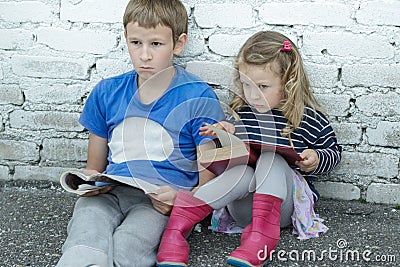 Wondering sibling children sitting on asphalt ground with books in hands Stock Photo