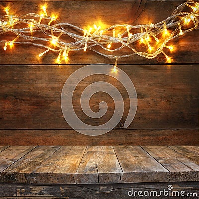 Wood board table in front of Christmas warm gold garland lights on wooden rustic background. filtered image. selective focus Stock Photo