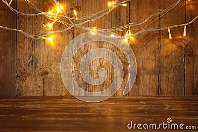 wood board table in front of Christmas warm gold garland lights on wooden rustic background. glitter overlay Stock Photo