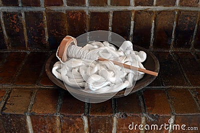 Wood bowl filled with white cotton roving and a spindle on a brick background Stock Photo