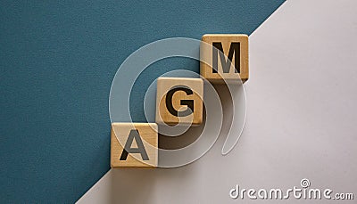 Wood cubes with acronym `AGM` - `annual general meeting` on a beautiful white and blue background. Business concept, copy spac Stock Photo