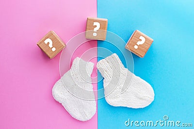 Wood cubes with question marks and pair of cute knitted baby socks on yellow-blue background. Gender of the baby. Boy or girl. Stock Photo