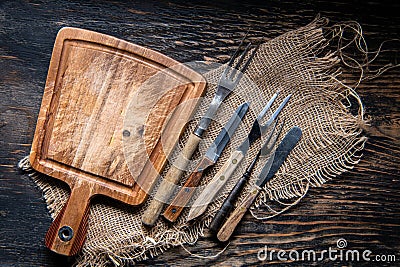 Wood cutting board with a piece of burlap, knives and forks on wooden table with copy space, top view Stock Photo