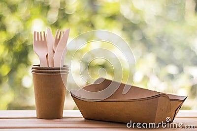 Wood forks and knives in craft cups, paper plates, natural green blurred background. Eco-friendly disposable kitchenware utensils Stock Photo