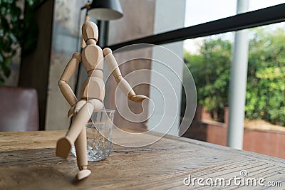 Wood man is sitting cross-leg on a glass of water Stock Photo