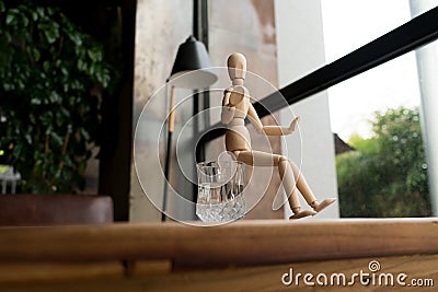 Wood man is sitting on a glass of water Stock Photo