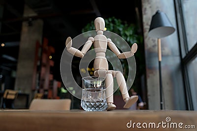 Wood man is sitting on a glass of water Stock Photo