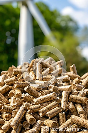 Wood pellets stacked prominently in front of a grand and powerful wind turbine structure Stock Photo