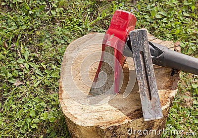 A wood splitting maul with a metal wedge on top of a wooden log Stock Photo