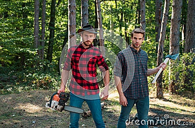 Woodcutters with chainsaw lumberjacks with axe. Hipsters men on serious face with axe. Lumberjack brutal and bearded Stock Photo