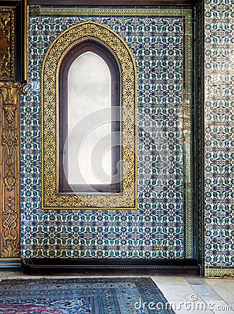 Wooden arched window framed by golden floral pattern ornaments over ceramic tiles wall with floral blue patterns Stock Photo