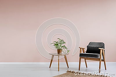 Wooden armchair with gray upholstery and a side table in a pastel pink living room interior with place for a bookcase. Real photo. Stock Photo