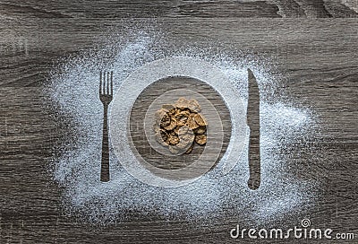 On a wooden background flour powder powdered snow silhouette plate plate fork knife appliances poured corn cereal flakes Stock Photo