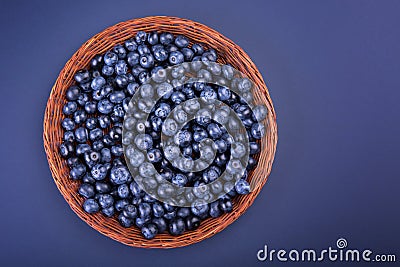 A wooden basket with juicy and bitter blueberries on a dark purple background, top view. A crate full of berries. Stock Photo