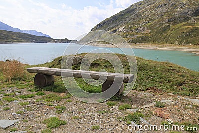 Wooden bench, bench at the reservoir Monte Spluga, at the SplÃ¼gen Pass, and surrounding mountains in summer Stock Photo