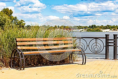 A wooden bench on the Dnipro embankment against the background of tall grass, a wide river of light cloudy sky Stock Photo