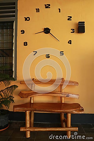 Wooden bench near yellow wall. Vintage wooden bench under the wall clock Stock Photo