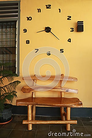 Wooden bench near yellow wall. Vintage wooden bench under the wall clock Stock Photo
