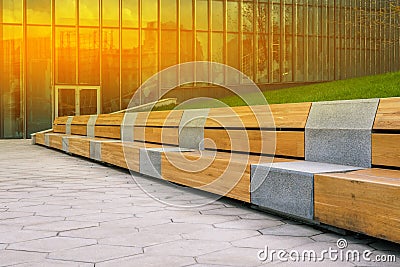 Wooden bench and tiled walkway. Office building for the work of company employees. Glass walls of a building with Stock Photo