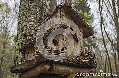 Wooden birdhouse attached to birch trunk made of boards and twigs with double level roof, feeder-balcony, braided twigs fence Stock Photo