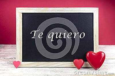 Wooden blackboard with red hearts and written sentence in Spanish Te quiero, which means I love you Stock Photo