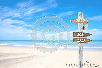 Wooden blank sign with text 2020 and 2021, Over Blurred blue sea and sand beach with cloudy blue sky Stock Photo