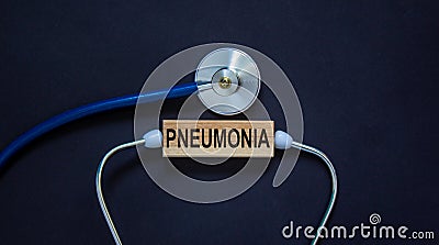 Wooden block with word `pneumonia` and stethoscope on black background. Medical concept Stock Photo