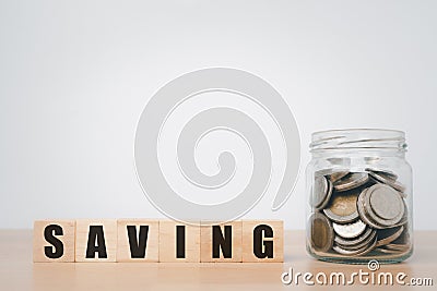 Wooden blocks cube with word saving and coin in glass jar on wooden table Stock Photo