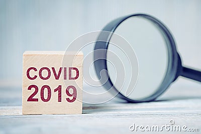 Wooden blocks with the inscription virus - COVID-19 next to a magnifying glass Stock Photo