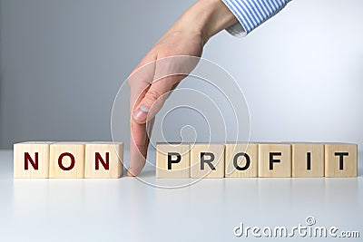 Wooden blocks with letters making Non Profit text. Woman`s hand between non and profit Stock Photo
