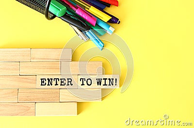 Wooden blocks stacked next to pens and pencils on a yellow background. ENTER TO WIN text on a wooden block. Stock Photo