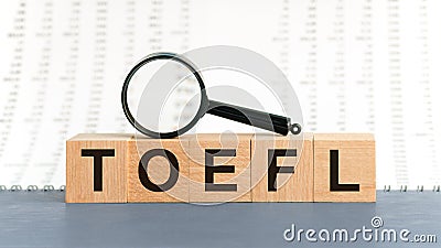 On wooden blocks under a magnifying glass text: TOEFL. Educational concept. TOEFL - words from wooden blocks with letters, Test of Stock Photo