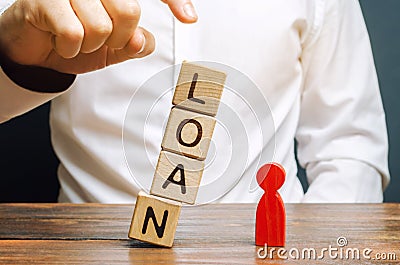 Wooden blocks with the word Loan fall on a miniature person. The concept of large lending rates for property and business. Lending Stock Photo