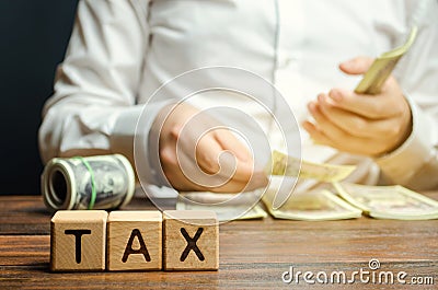 Wooden blocks with the word Tax and a businessman who counts money. The concept of time payment of taxes. Tax rates. Taxation / Stock Photo