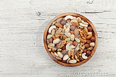 Wooden bowl with mixed nuts on white table from above. Healthy food and snack. Walnut, pistachios, almonds, hazelnuts and Stock Photo