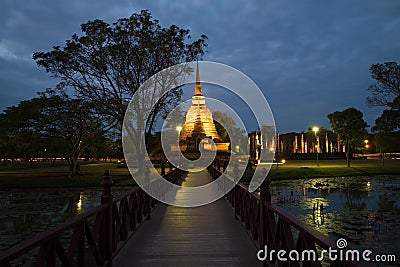 The wooden bridge conducting to ruins of the ancient Buddhist temple of Wat Sa Si in evening twilight. Sukhothai, Thailand Stock Photo