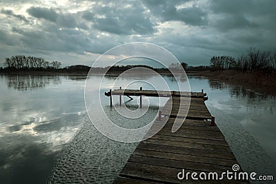 Wooden bridge on the lake, rainy clouds on the evening sky Stock Photo